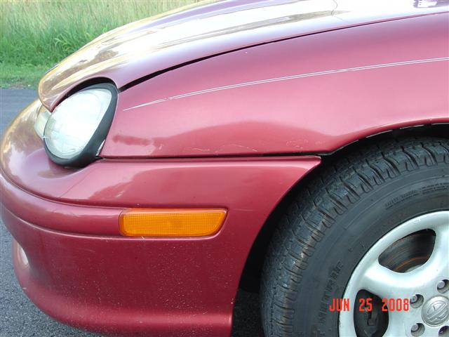 Front corner of a red 1997 Dodge Neon, showing the headlight, fender, and tire