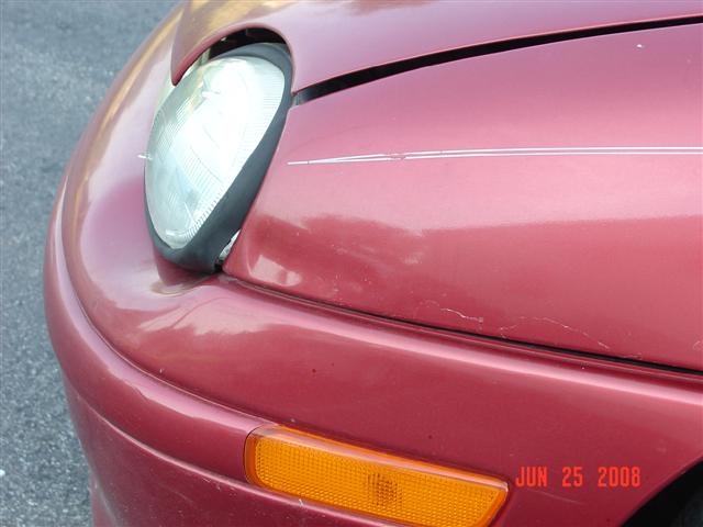 Red 1997 Dodge Neon front fender with a headlight and amber turn signal. Faint pinstripes are visible on the hood