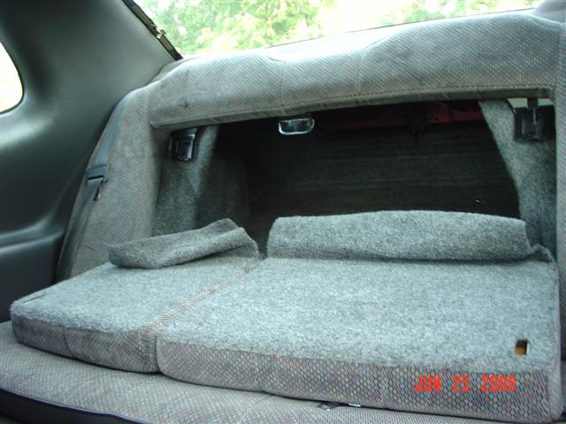 Rear seat folded down in a car interior, showing the trunk area behind it. Fabric upholstery is grey