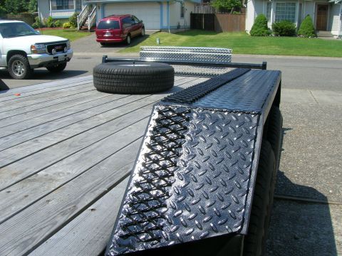 1996 Ford Bronco - A trailer deck is shown with a spare tire and a toolbox, while a white GMC pickup truck is parked nearby.