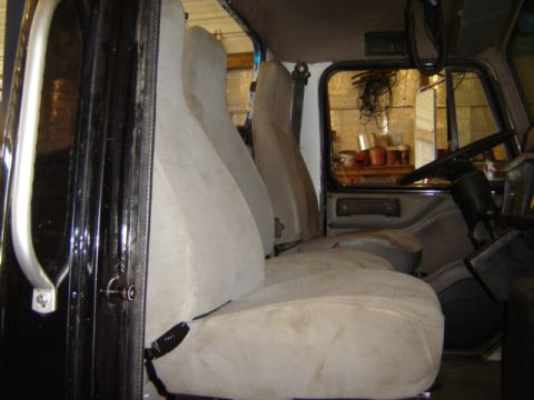 1992 Ford Bronco - The interior of a truck shows tan seats and the driver's side controls, with a cluttered shelf visible through the window.
