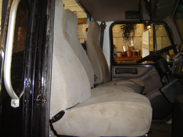 Truck interior with two rows of tan seats, steering wheel, and door panel visible. A shelf with items is seen through the side window
