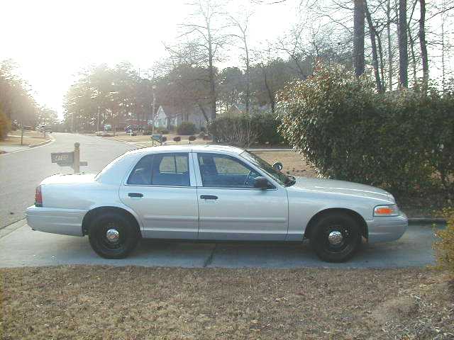 Silver Crown Victoria sedan with black steel wheels and spotlight, side view in residential driveway