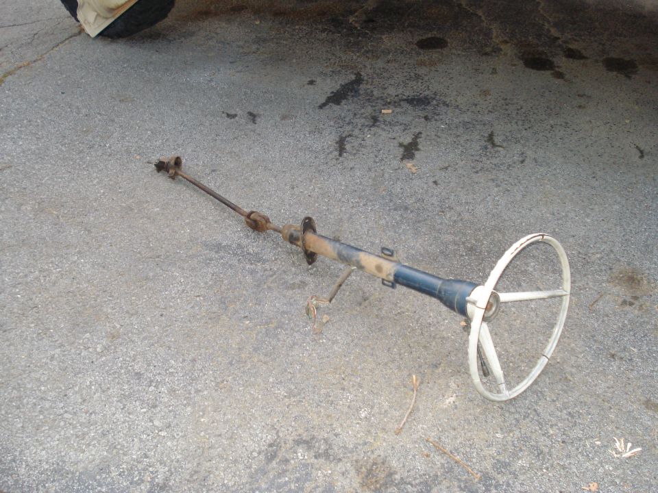 Steering column with a white three-spoke wheel lies on asphalt