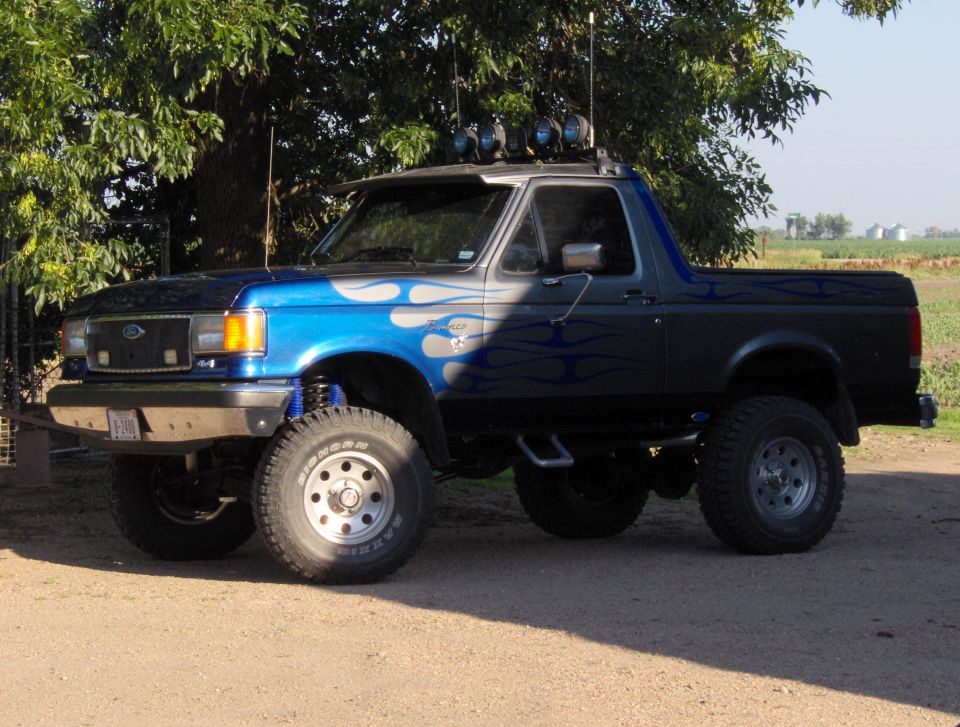 Blue and black lifted Ford Bronco with flame decals, off-road tires, and roof-mounted lights