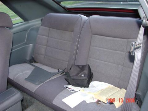 1984 Ford Mustang - The rear interior of a car shows the back seat with a small bag and an open book resting on it.