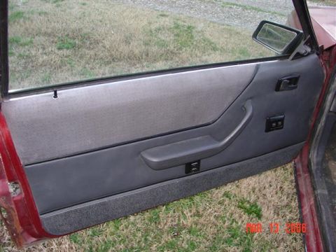 1984 Ford Mustang - The interior door panel of a 1984 Ford Mustang shows gray fabric and dark gray plastic trim.