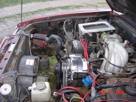 1984 Ford Mustang - The engine bay of a red vehicle shows various components, including the radiator, air filter, and alternator.