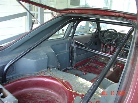 1984 Ford Mustang - The interior of the vehicle shows a roll cage and a partially disassembled cabin, stripped-down cabin.