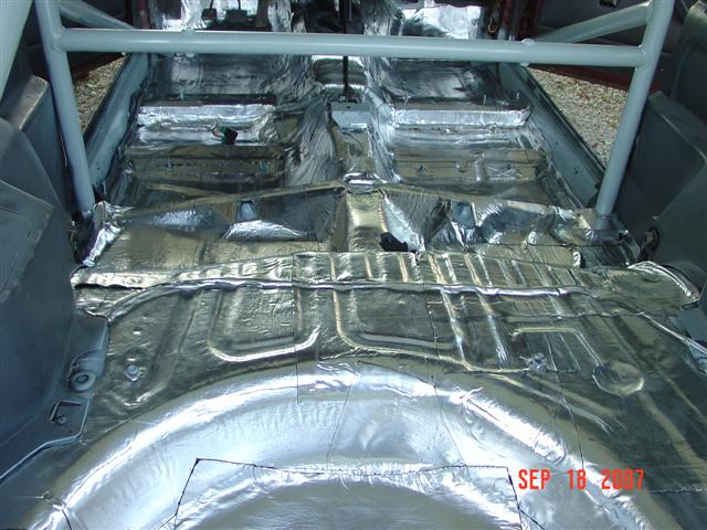 Car interior floor covered in silver sound deadening material, with a roll cage visible