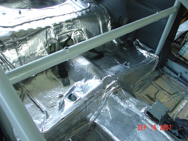 Car interior with silver sound deadening material applied to floor and rear panels, plus a roll bar
