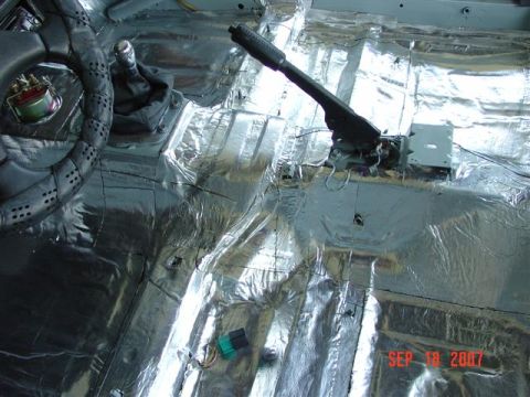 1984 Ford Mustang - The interior of a car is covered in silver sound deadening material, with a steering wheel and shifter visible.