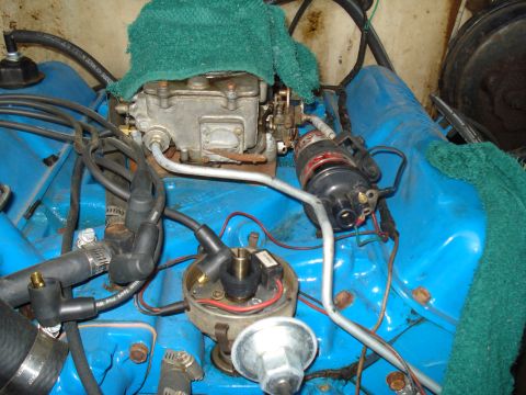 1967 Ford F-250 - Close-up view of engine wiring, distributor, and carburetor, with blue valve covers and green towels covering parts of the engine.