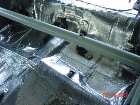 1984 Ford Mustang - The interior floor of a vehicle is covered in sound deadening material, with a roll bar visible.