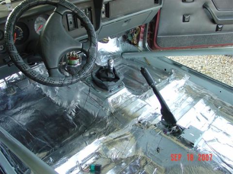 1984 Ford Mustang - The interior of a car is being prepped for sound deadening, revealing the bare metal floor and dashboard components.