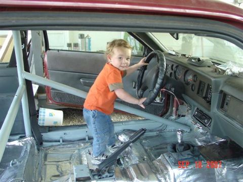 1984 Ford Mustang - A young child sits behind the steering wheel of a 1984 Ford Mustang, which appears to be undergoing modifications with a roll cage and soun…