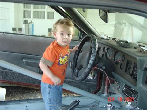 1984 Ford Mustang - Child in the driver's seat of a 1984 Ford Mustang, with roll cage visible.