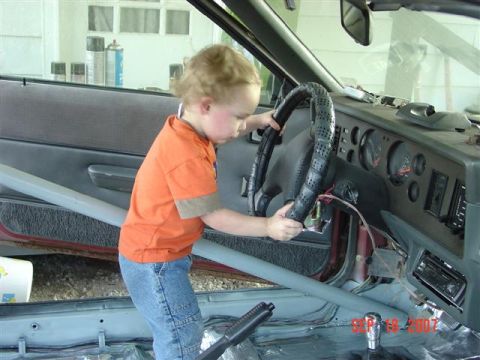 1984 Ford Mustang - A young child grips the steering wheel of a car, seemingly exploring the interior.