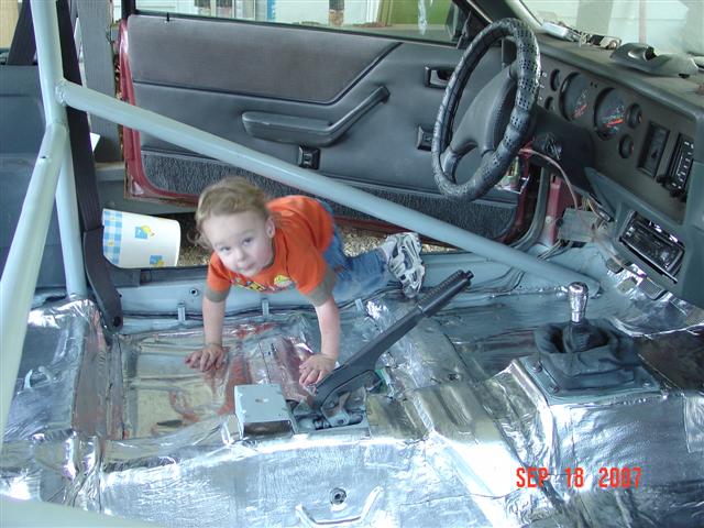 Kid crawling on floor of car with sound deadening material installed. Roll cage visible