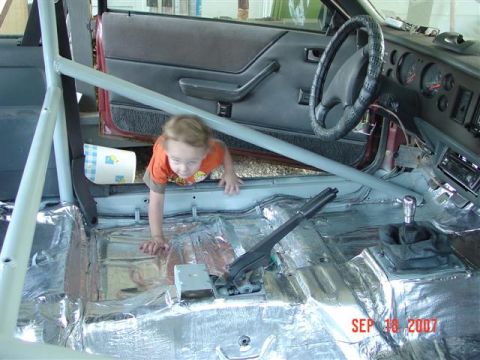 1984 Ford Mustang - A child crawls inside the interior of a 1984 Ford Mustang, which has been fitted with a roll cage and sound deadening material.