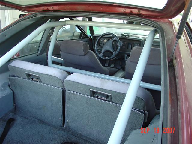 Red 1984 Ford Mustang interior with a grey roll cage, grey seats, and a black steering wheel