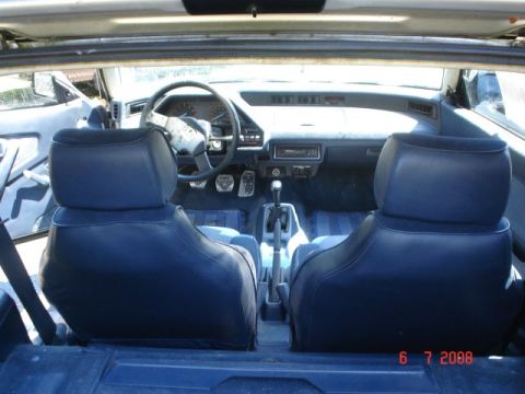 1990 Ford Bronco - The interior of a car, viewed from the rear seats, shows dark blue bucket seats, a dashboard with a steering wheel, and a manual transmissi…