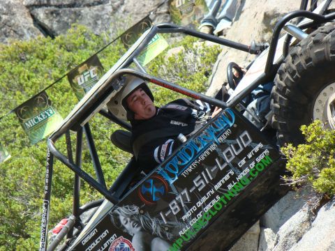 1989 Ford Bronco - A man wearing a helmet is in the driver's seat of a custom off-road buggy, which is tilted on a rocky incline. The buggy has a large tire a…