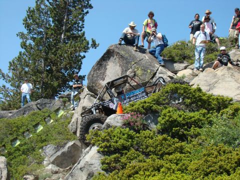 1989 Ford Bronco - A heavily modified off-road Bronco is shown navigating a steep, rocky incline. Several spectators are visible on the rocks above, watching…