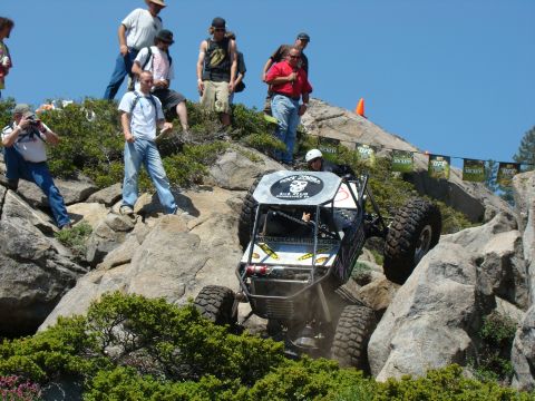 1989 Ford Bronco - A custom-built off-road buggy with large tires navigates a rocky incline under a clear blue sky, with spectators watching from above.
