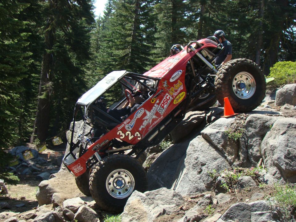 Red off-road vehicle with large tires climbing over rocks