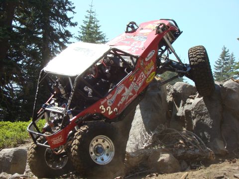 1989 Ford Bronco - A custom red off-road buggy with large tires is navigating a rocky incline, with its front right tire high in the air. The vehicle features…
