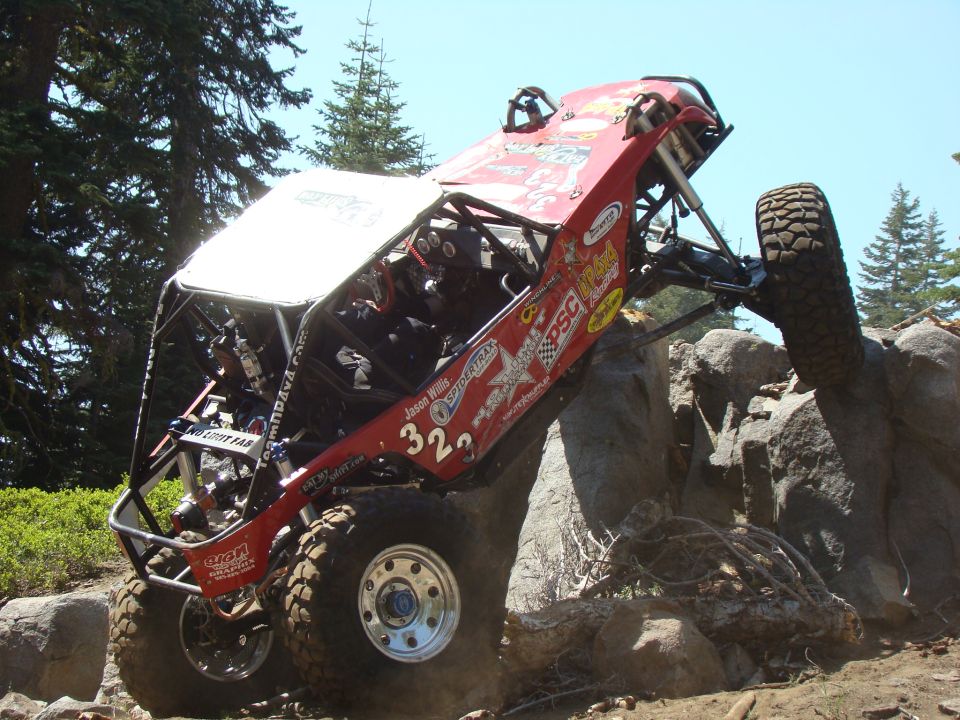 Red off-road buggy climbing rocks, front right tire raised high.