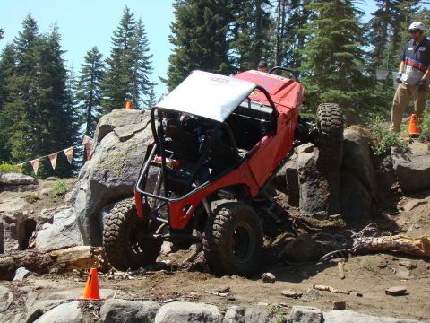 1989 Ford Bronco - A red off-road buggy is navigating a rocky, wooded terrain. The vehicle is tilted at a steep angle, with its front tire high on a boulder a…