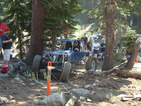 1989 Ford Bronco - A custom blue off-road buggy with large tires sits on a dirt trail surrounded by trees. Several people are gathered around watching the veh…
