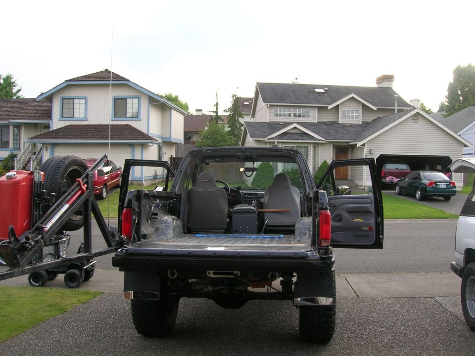 Black lifted Ford SUV from rear with top removed, stripped interior and mud-terrain tires in driveway
