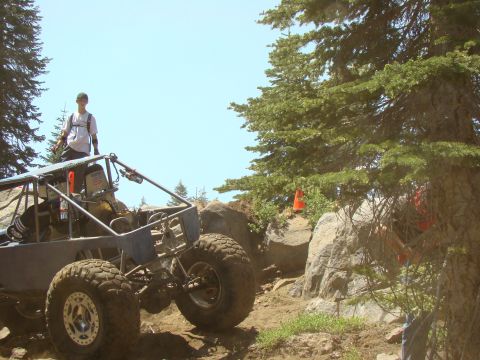 1989 Ford Bronco - A custom off-road buggy with large tires is navigating a rocky, wooded trail. A person stands on the buggy's roll cage, looking out at the…