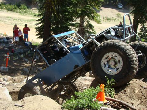 1989 Ford Bronco - A custom-built off-road buggy with large tires navigates a steep, rocky incline. Several people stand nearby watching the action.