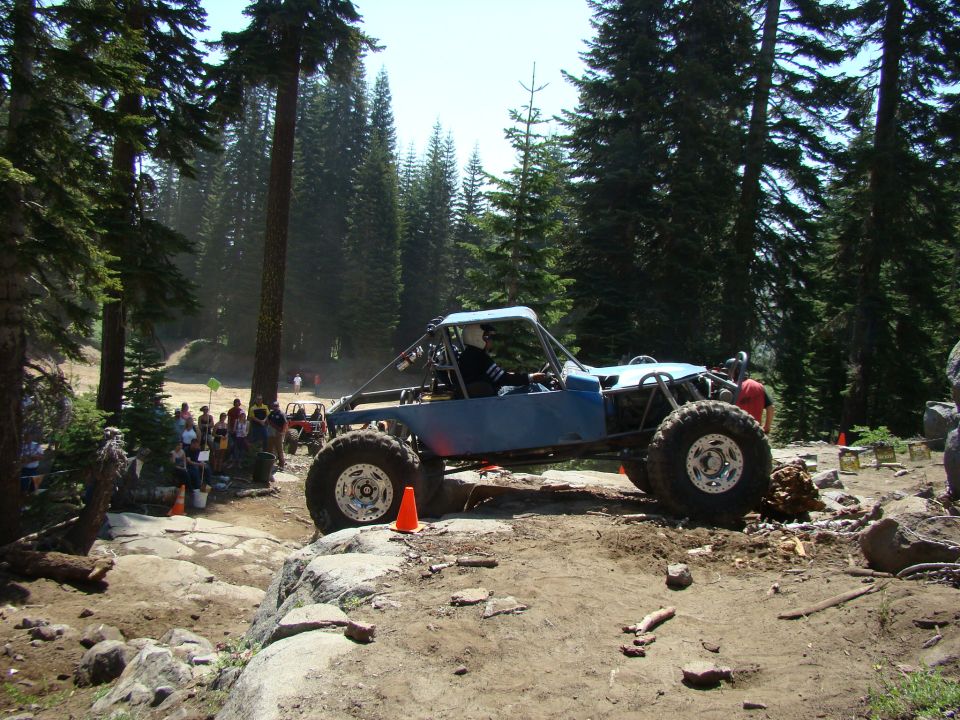 Blue custom off-road buggy on a rocky trail with trees and spectators.