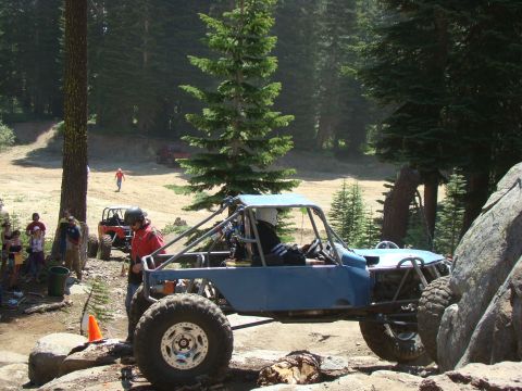 1989 Ford Bronco - A custom blue off-road buggy with a driver wearing a helmet navigates a rocky trail with a group of spectators and other vehicles nearby in…