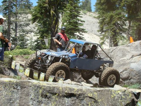 1989 Ford Bronco - Off-road vehicle driving on a dirt path with trees in the background.