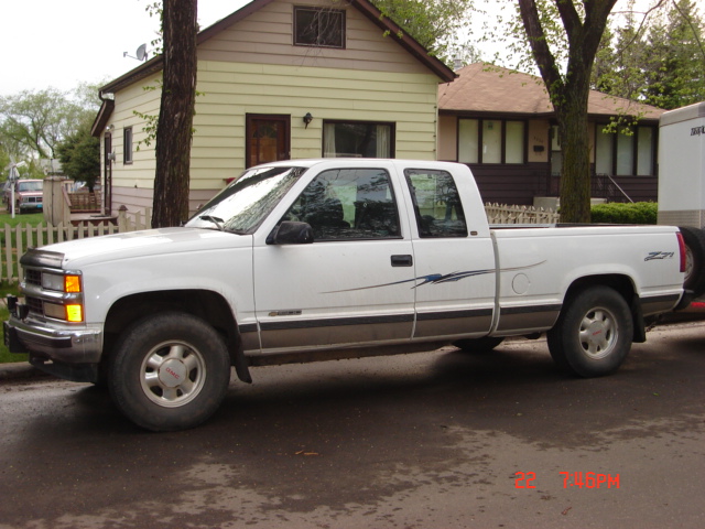 White Chevrolet extended-cab pickup parked at curb, driver's side view