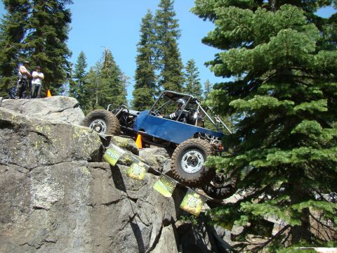 1989 Ford Bronco - A custom blue off-road buggy navigates a challenging rocky obstacle course, with event flags visible on the rocks.