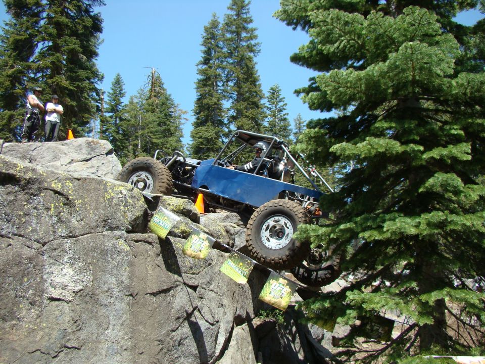 Blue off-road buggy climbing rocky terrain with flags hanging