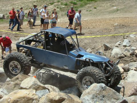 1989 Ford Bronco - A custom-built buggy tackles a rocky obstacle course with spectators watching.