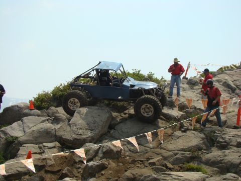 1989 Ford Bronco - A custom blue off-road buggy navigates a rocky course with spectators observing the action.