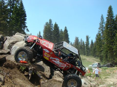 1989 Ford Bronco - Custom off-road buggy navigates a steep, rocky trail with a pickup truck visible in the distance.