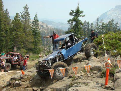 1989 Ford Bronco - Two off-road vehicles navigate a rocky course with spectators watching.