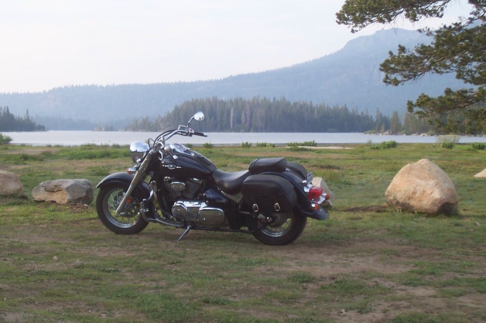 Black motorcycle with saddlebags parked on grass near a lake and mountains