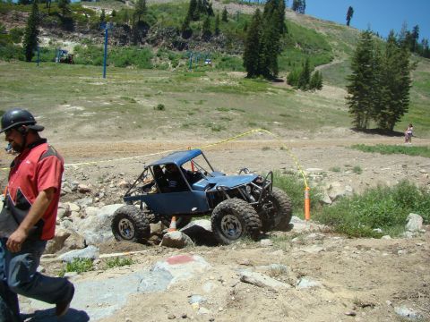 1989 Ford Bronco - A custom-built blue off-road buggy with a prominent roll cage is shown traversing a challenging, rocky course.