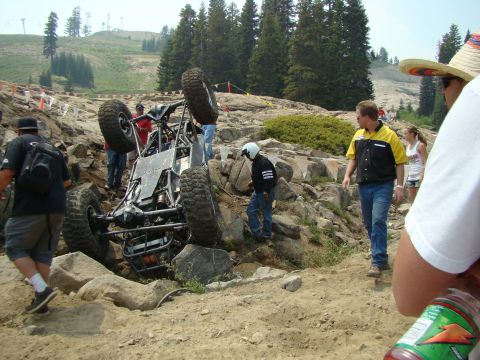 1989 Ford Bronco - An off-road buggy has overturned on a rocky course, with spectators observing the scene.